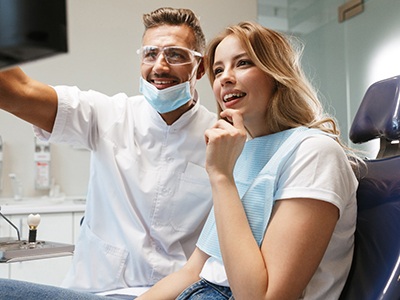A dentist and female patient review images of her smile on a nearby monitor