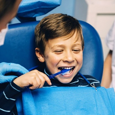 little boy brushing teeth in dental chair