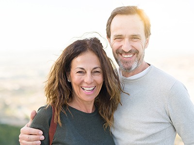 A middle-aged couple smiling while posing outside after seeing their Delta Dental in-network dentist in Frisco