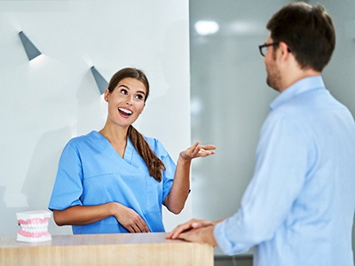 A female dental receptionist talking to a male patient from behind the front desk