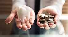 Person holding model tooth and coins in their hands