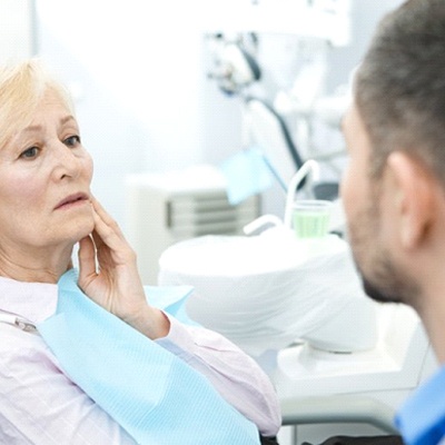 senior woman with dental implant pain talking to dentist