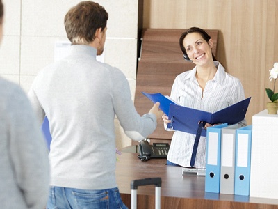 A female front desk receptionist smiling while helping a male patient prepare for his visit