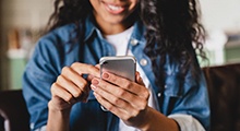 Woman in jean jacket smiling while looking at phone