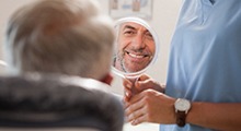 Man examining smile in mirror with emergency dentist in Frisco