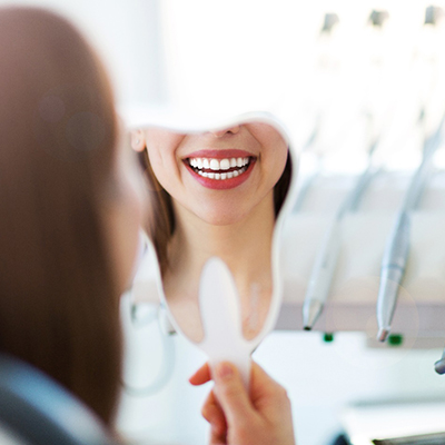 Woman with white teeth smiling in dentist's mirror